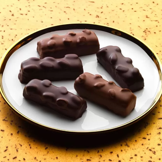 A white plate with a gold rim holds five rectangular chocolate bars with a bumpy texture, placed on a speckled yellow surface.