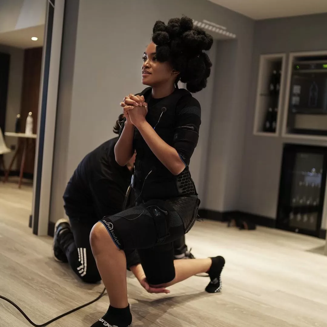 Woman lunging in a gym wearing a EMS (electro-muscle stimulation) with Personal Trainer