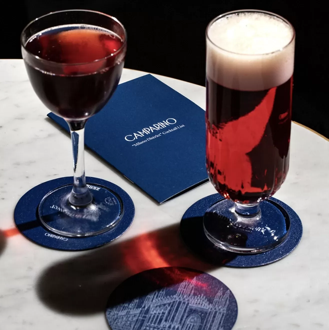Wine and beer served in glasses on branded coasters with menu on a table at Camparino in Galleria