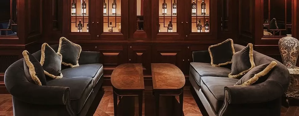 Two blue sofa's with cushions facing each other between two half moon coffee tables in front of wooden wine cabinet