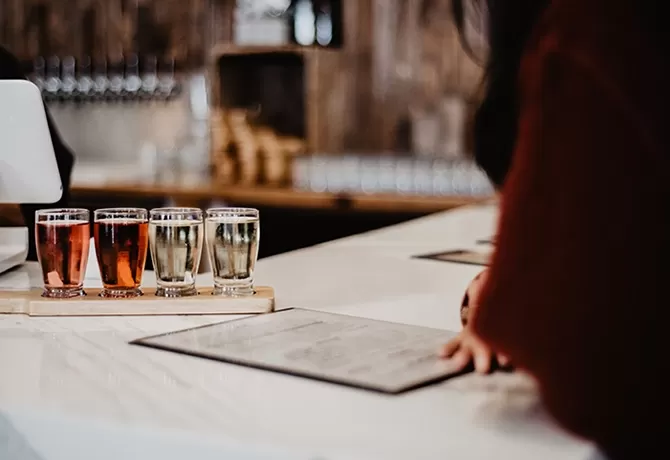 Cider tasting at a table with 8 small glasses of various ciders in wooden holder