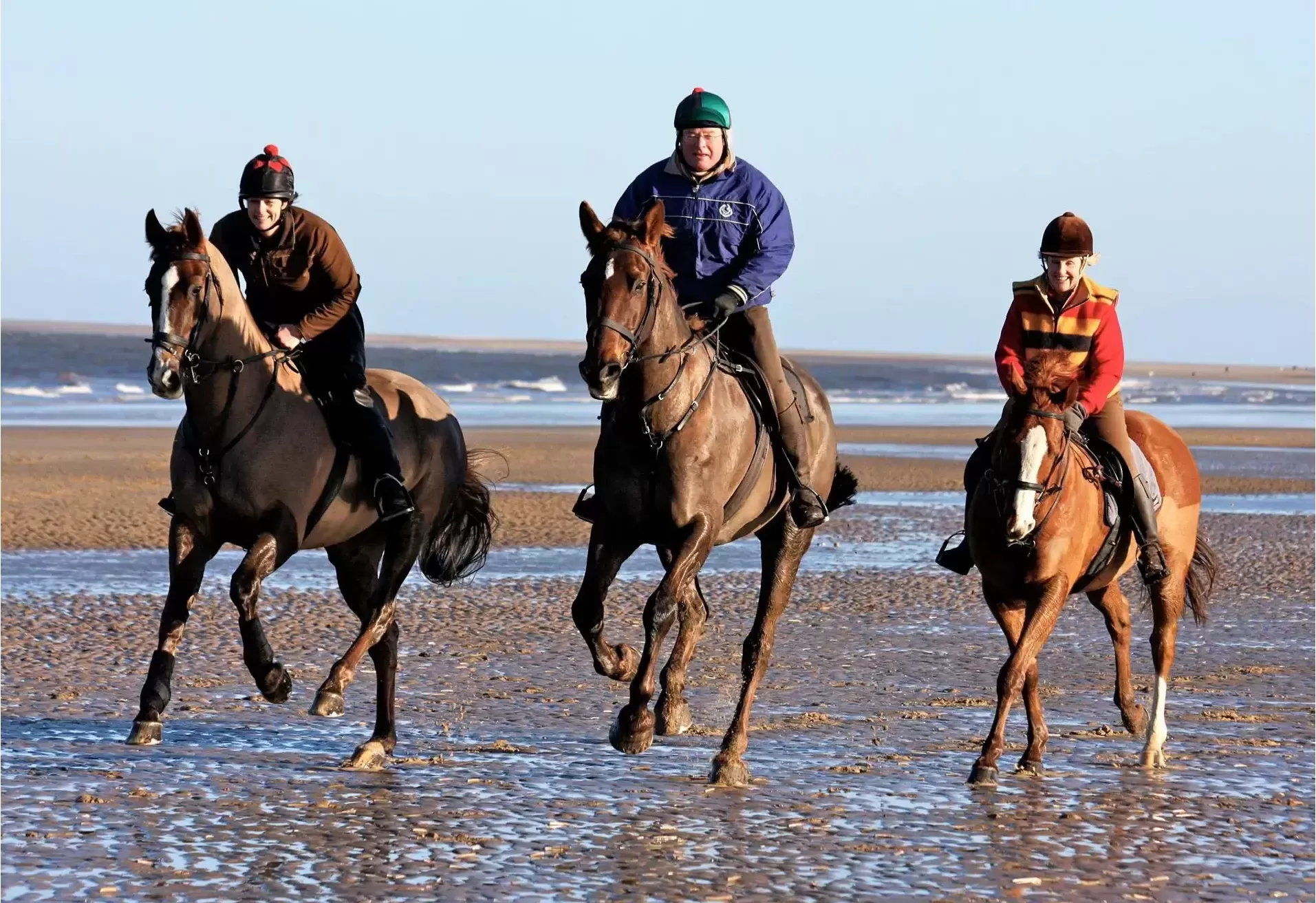 Three people racing horses on a beach