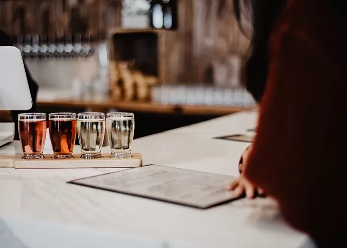 Cider tasting at a table with 8 small glasses of various ciders in wooden holder