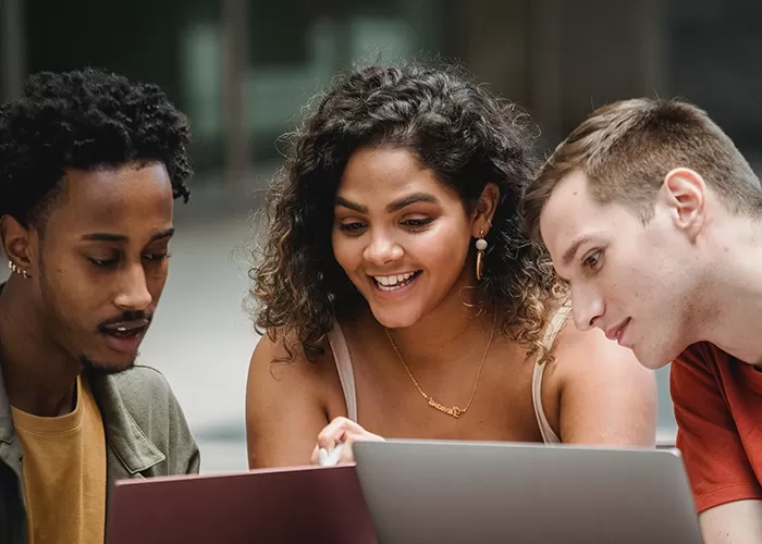 Three young adults smiling and looking at computer screens