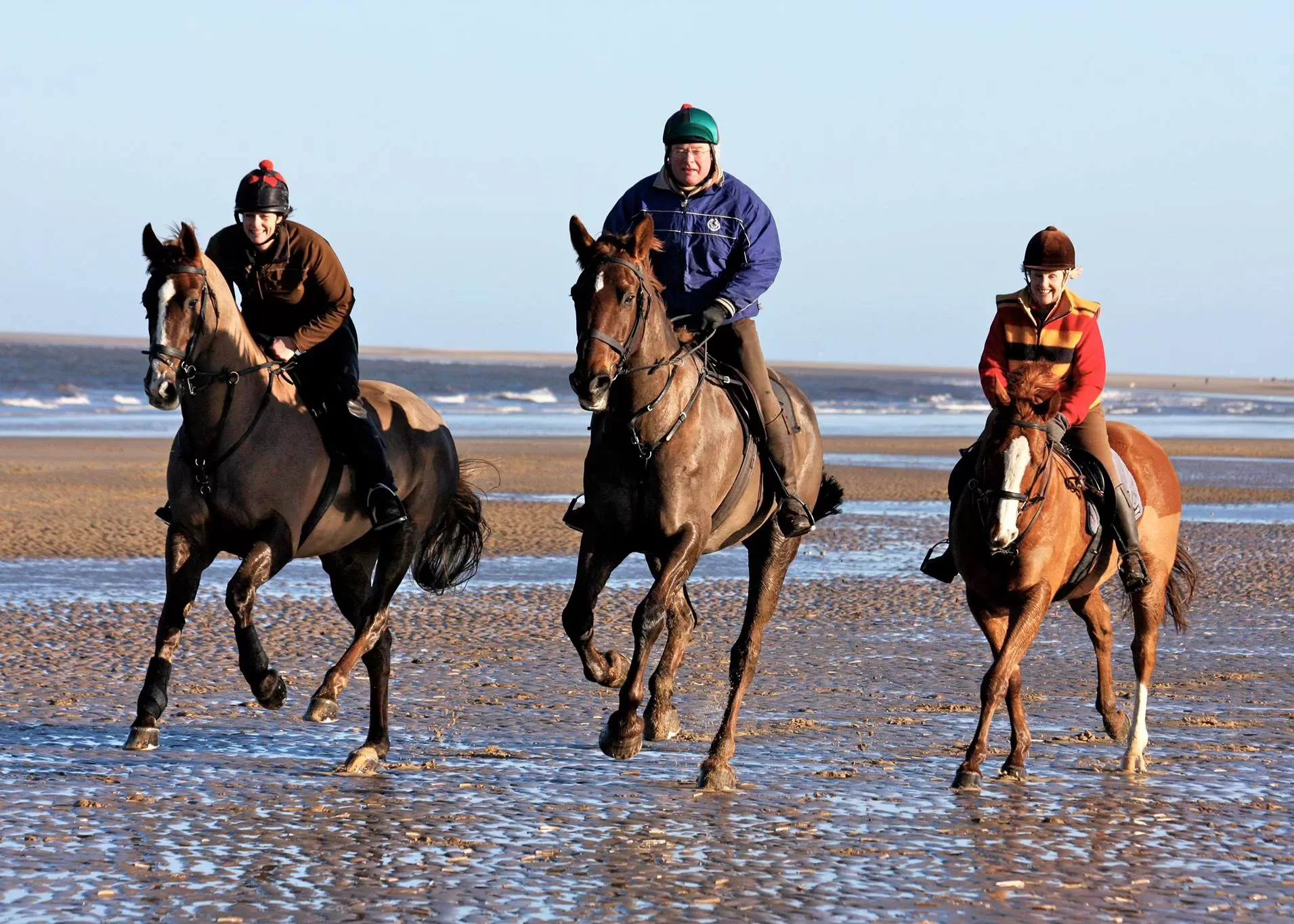 Three people racing horses on a beach