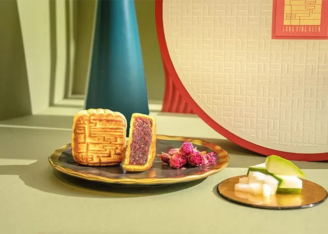 A plate holds two winter melon mooncakes next to an assortment box and a plate of garnises, showcasing a charming dessert arrangement.