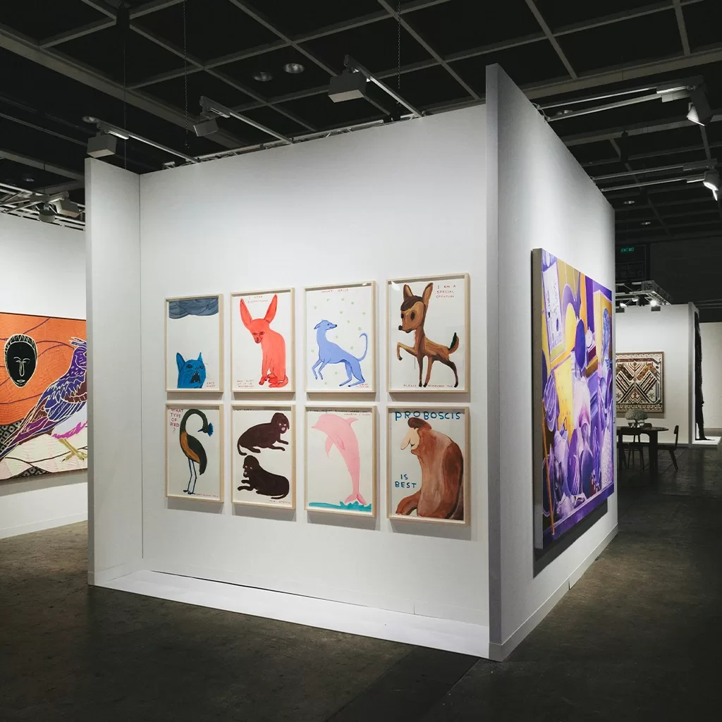 A modern art gallery features brightly colored animal paintings on white walls, including several playful, abstract animal figures arranged in a grid, with larger colorful artworks displayed nearby.