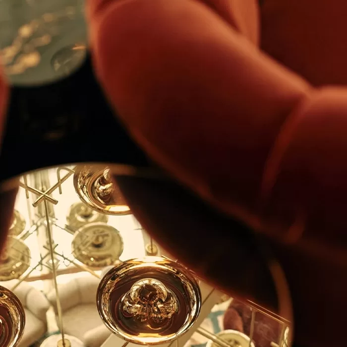 A close-up view of a hand holding a dark object, reflecting multiple bright, circular, golden lights in a mirrored surface, creating a symmetrical and abstract pattern.