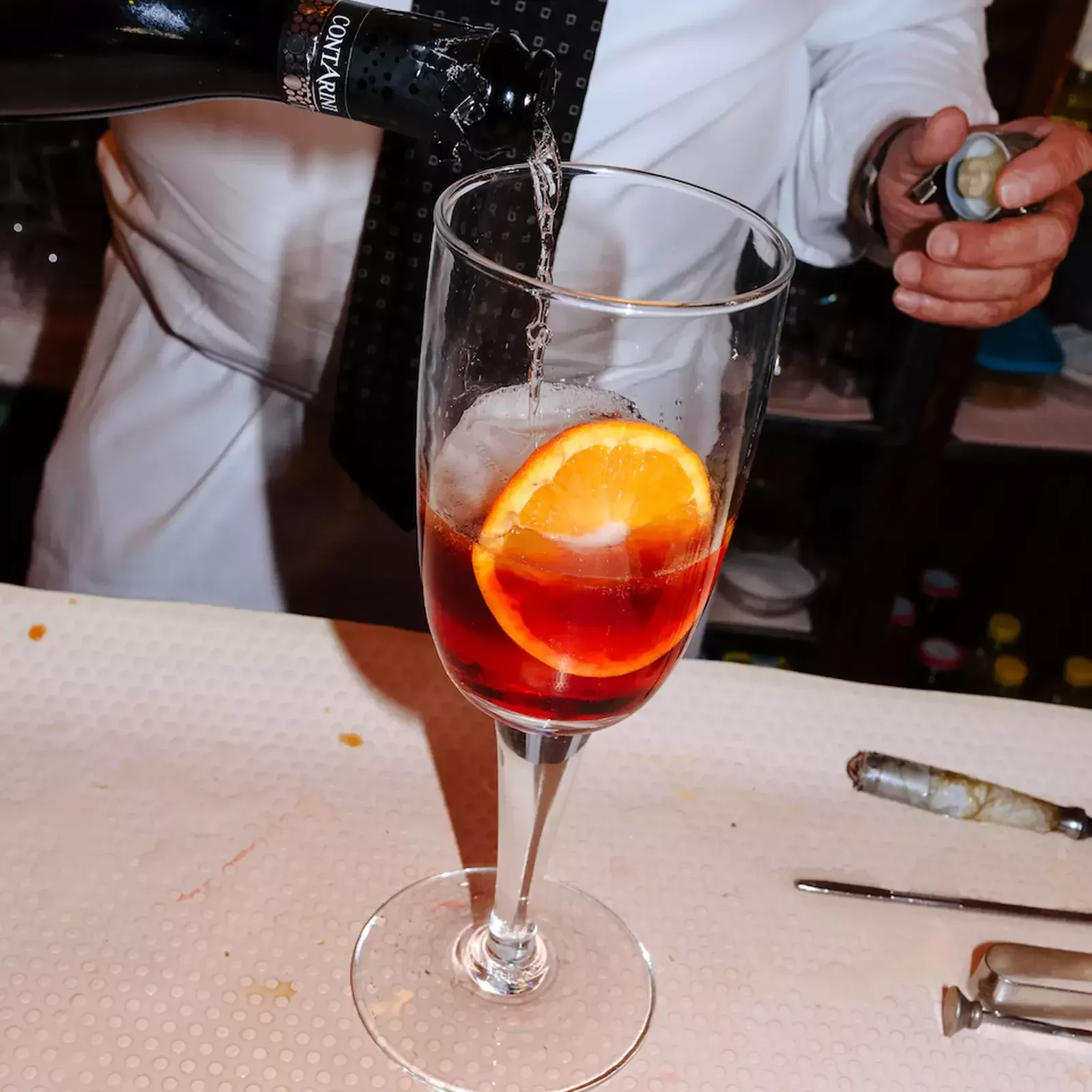 Waiter pouring cocktail into glass with orange garnish at Bar Basso, Milan