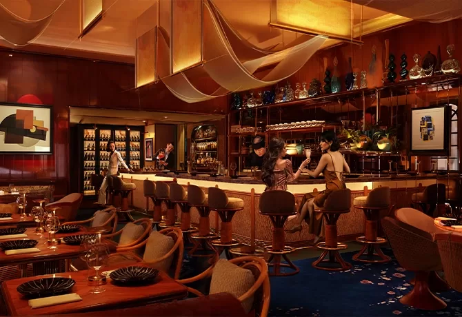 A stylish, warmly lit restaurant bar with elegant wooden furniture, abstract art on the walls, and several people sitting at the bar. Draped fabric hangs from the ceiling, creating a cozy and sophisticated atmosphere.