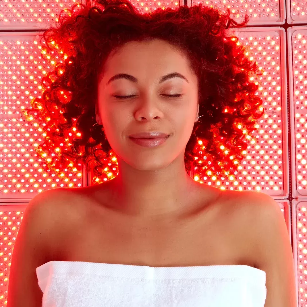 Woman lay down on a red lit bed receiving beauty treatment