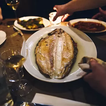 Open fired cooked fish dish served on a plate with white wine at BRAT, Soho, London