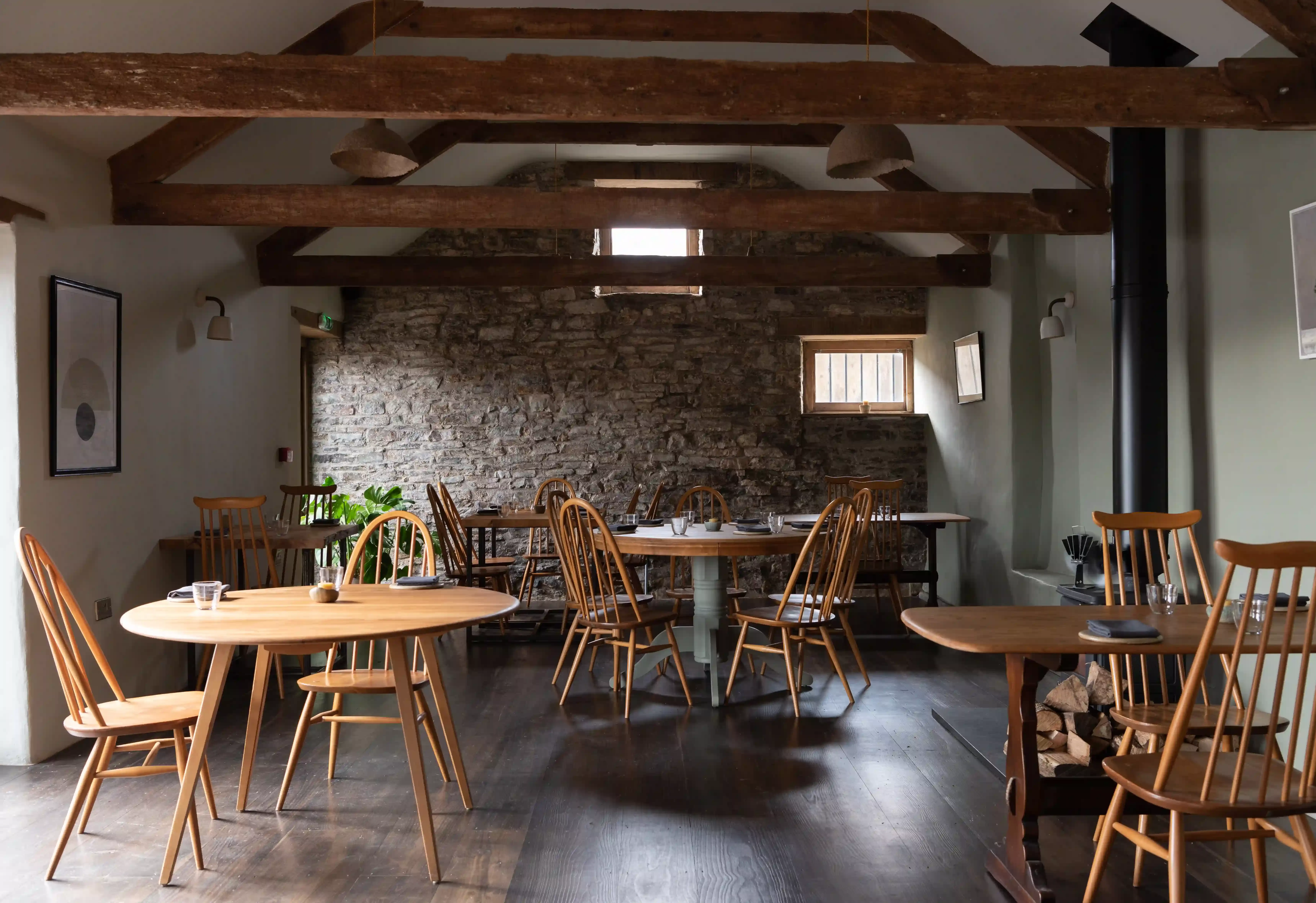 Quint cottage style restaurant interior with Cornish stone walls and round wooden tables under wooden beamed roof at Crocadon Farm, Cornwall
