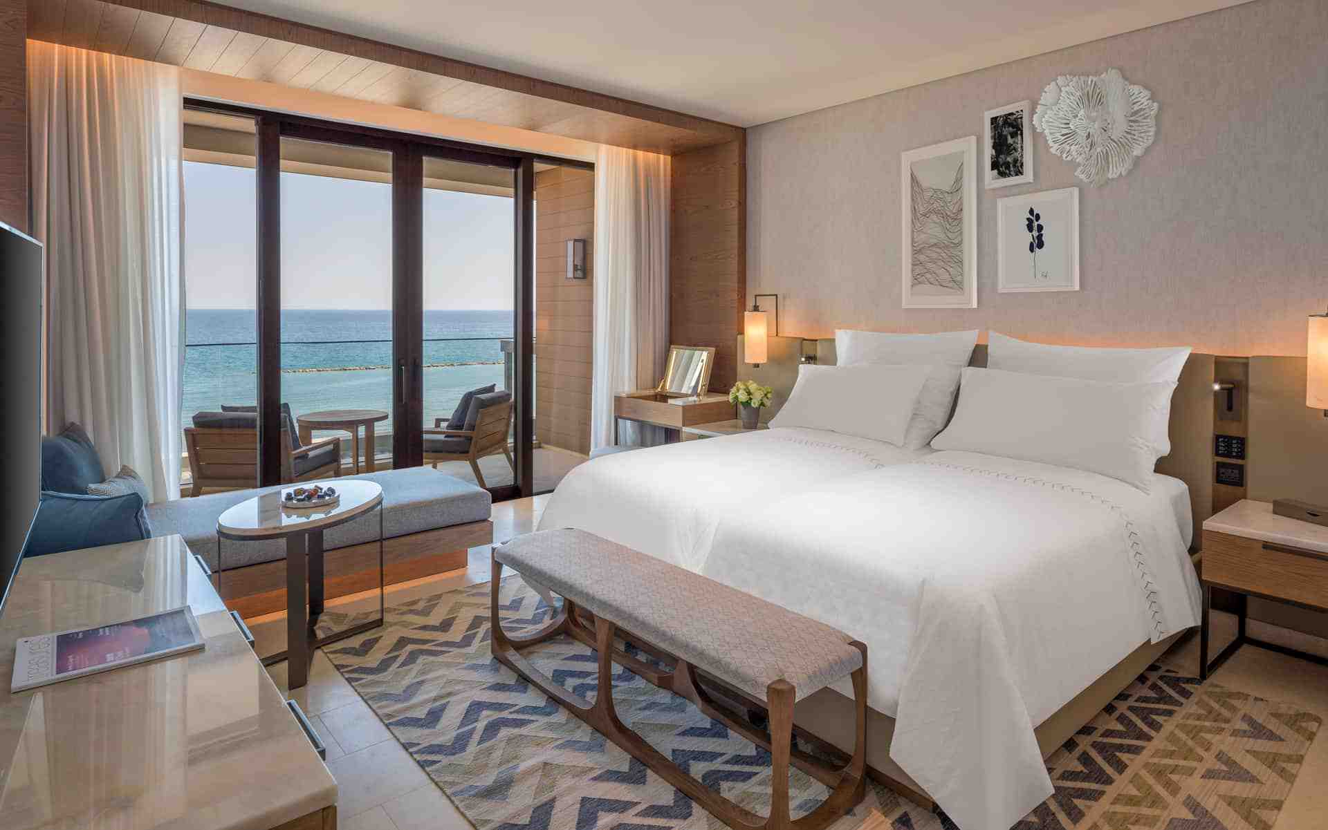 Hotel room with patterned rug, white twin bed and sea view balcony.