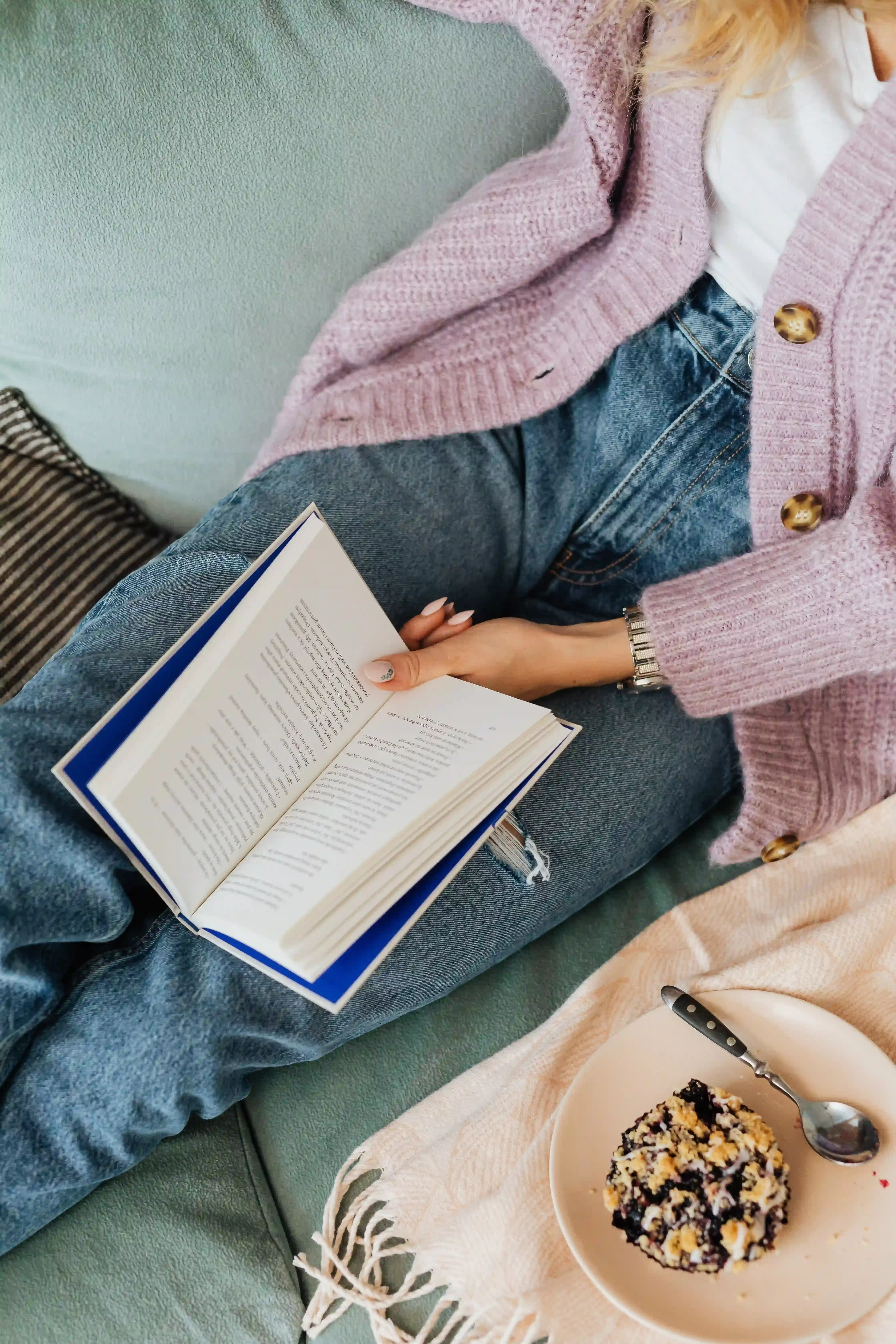 Women in jeans and cardigan reading a book with plate of breakfast