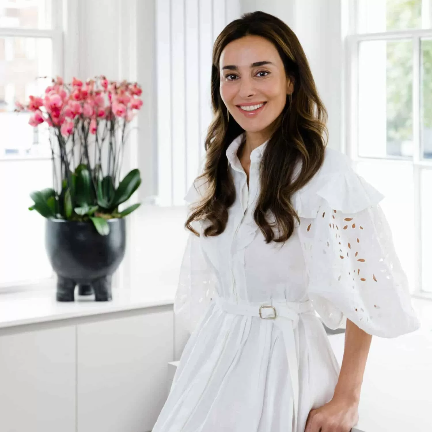 Dr Maryam Zamani in a white dress posing next to pink flowers