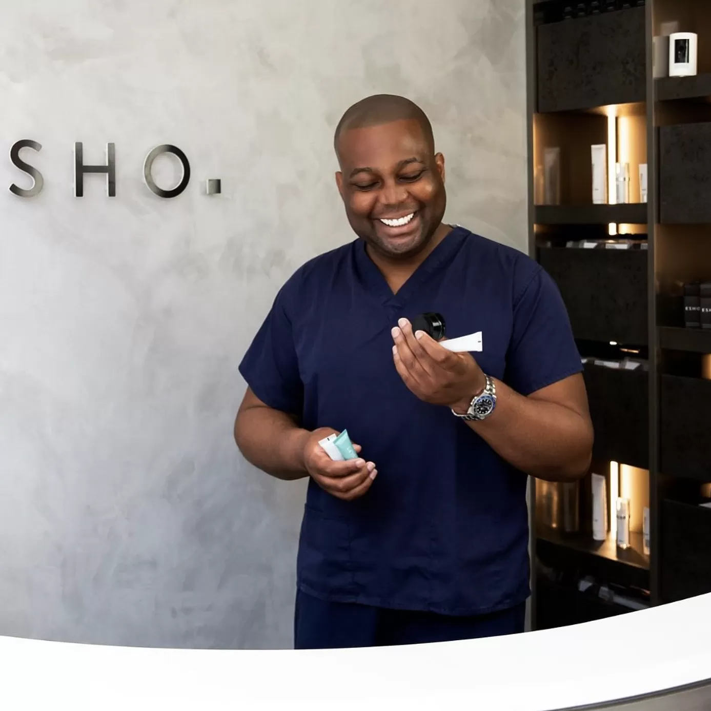 Dr Tijion Esho smiling in his clinic holding products