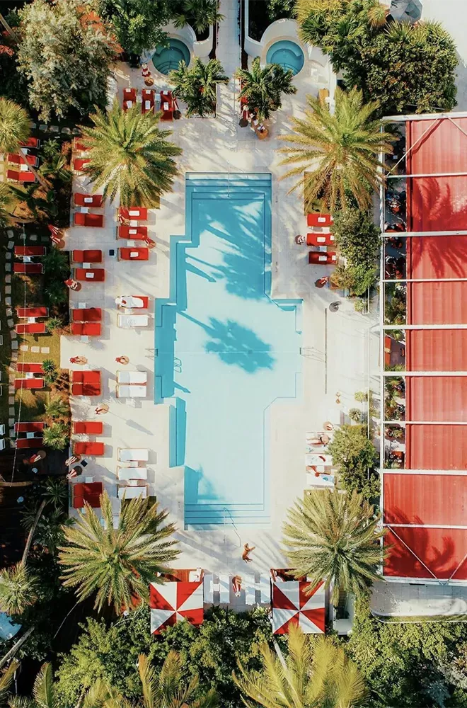 Birds eye view of swimming pool surrounded by palm trees and red and white sunlounges
