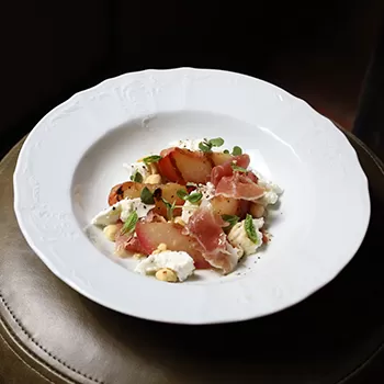 Peaches, ricotta, prosciutto served on a plate at Firebird, Soho, London