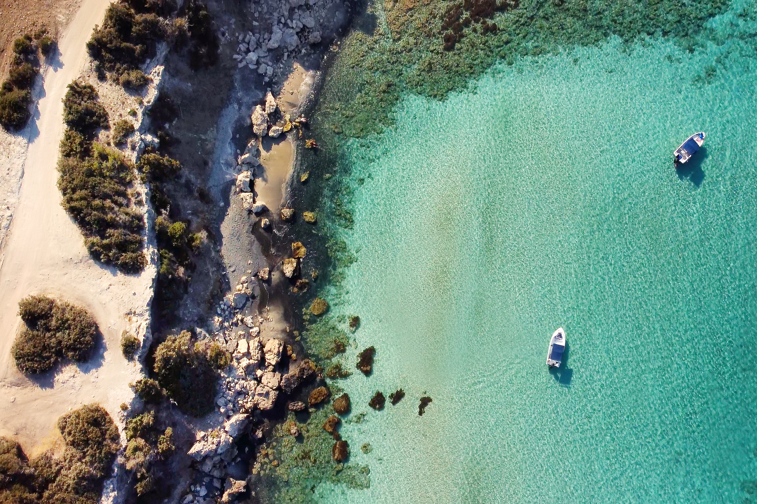 Birds eye view of clear sea with mossy beach with two boats.