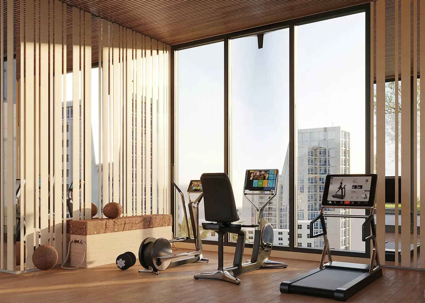 A modern gym room with large windows overlooking tall buildings, featuring a treadmill, two stationary bikes, exercise balls, and wooden decor elements on a wood floor.