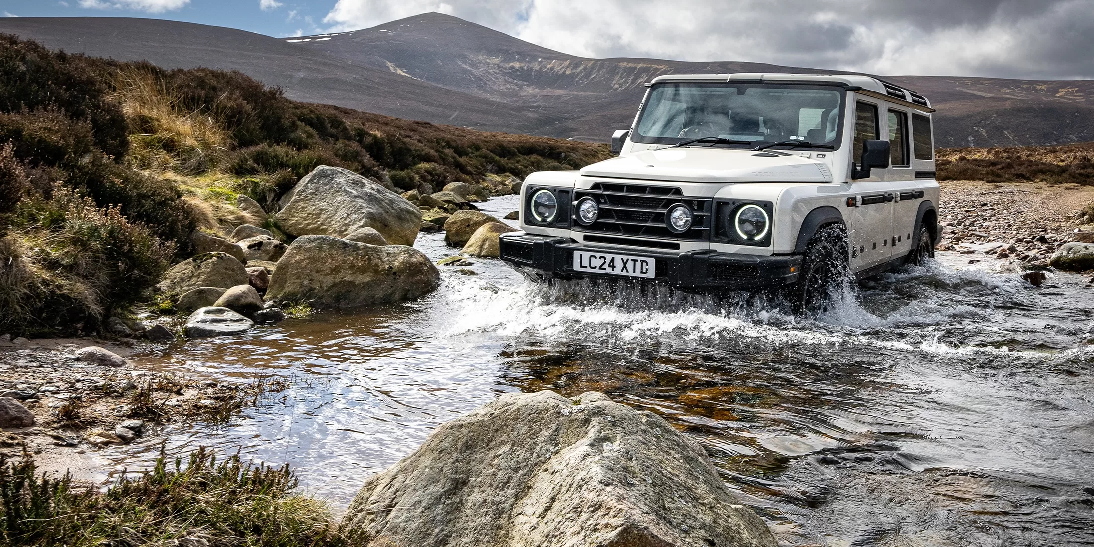 Birdeye eye view of the white INEOS Grenadier - ‘son of Defender’ car created by Sir Jim’s lieutenants off-road driving through water and rocks in the Cairngorms, Scotland.