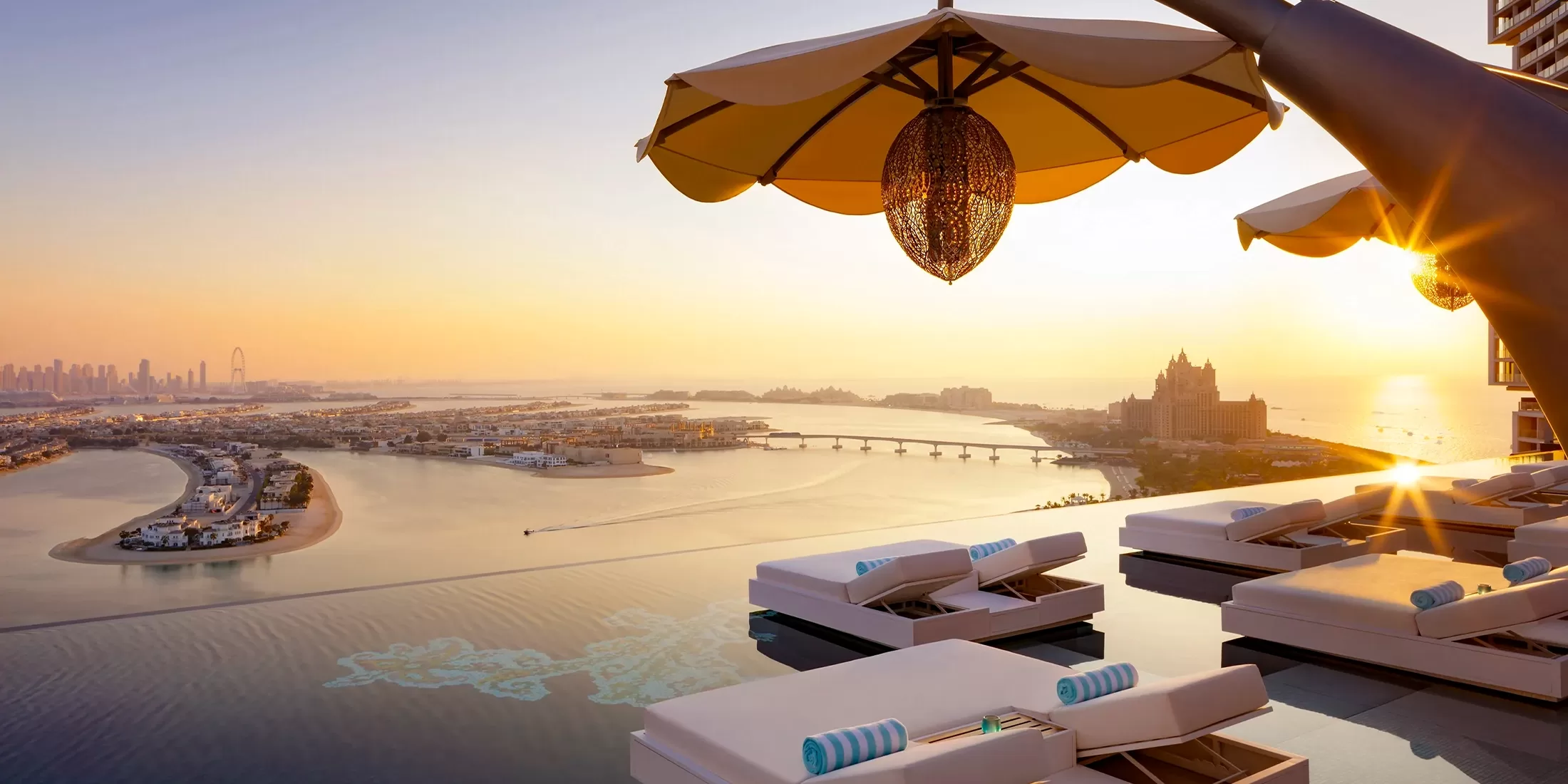 White loungers with turquoise pillows overlook beautiful sea and Dubai shoreline.