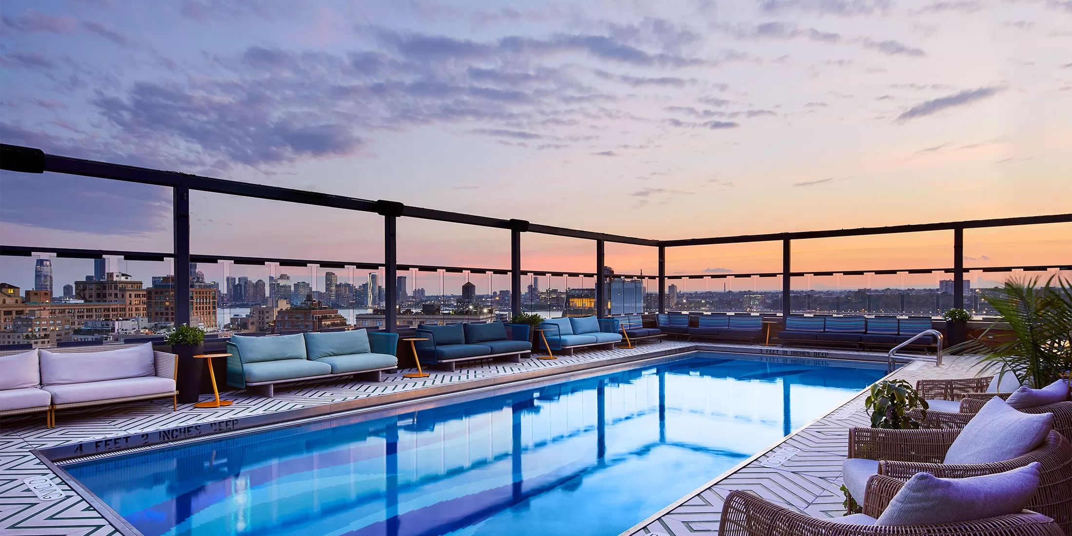 Crystal blue swimming pool with sofas and wicker chairs around it overlooking the New York Skyline.