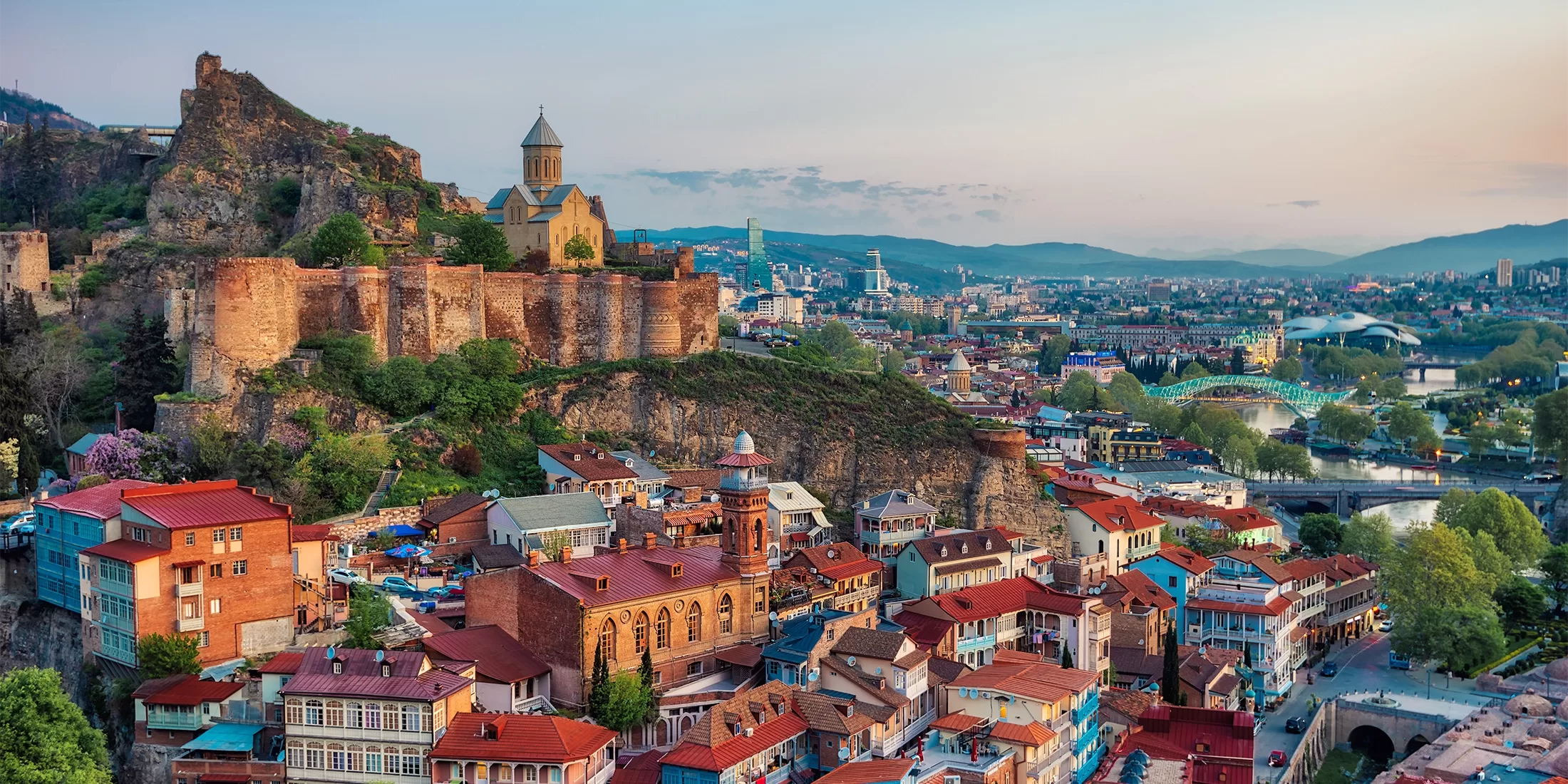 Birdseye view of beautiful buildings on a hill side in different colours including blue, rusted red and yellow in Tbilisi