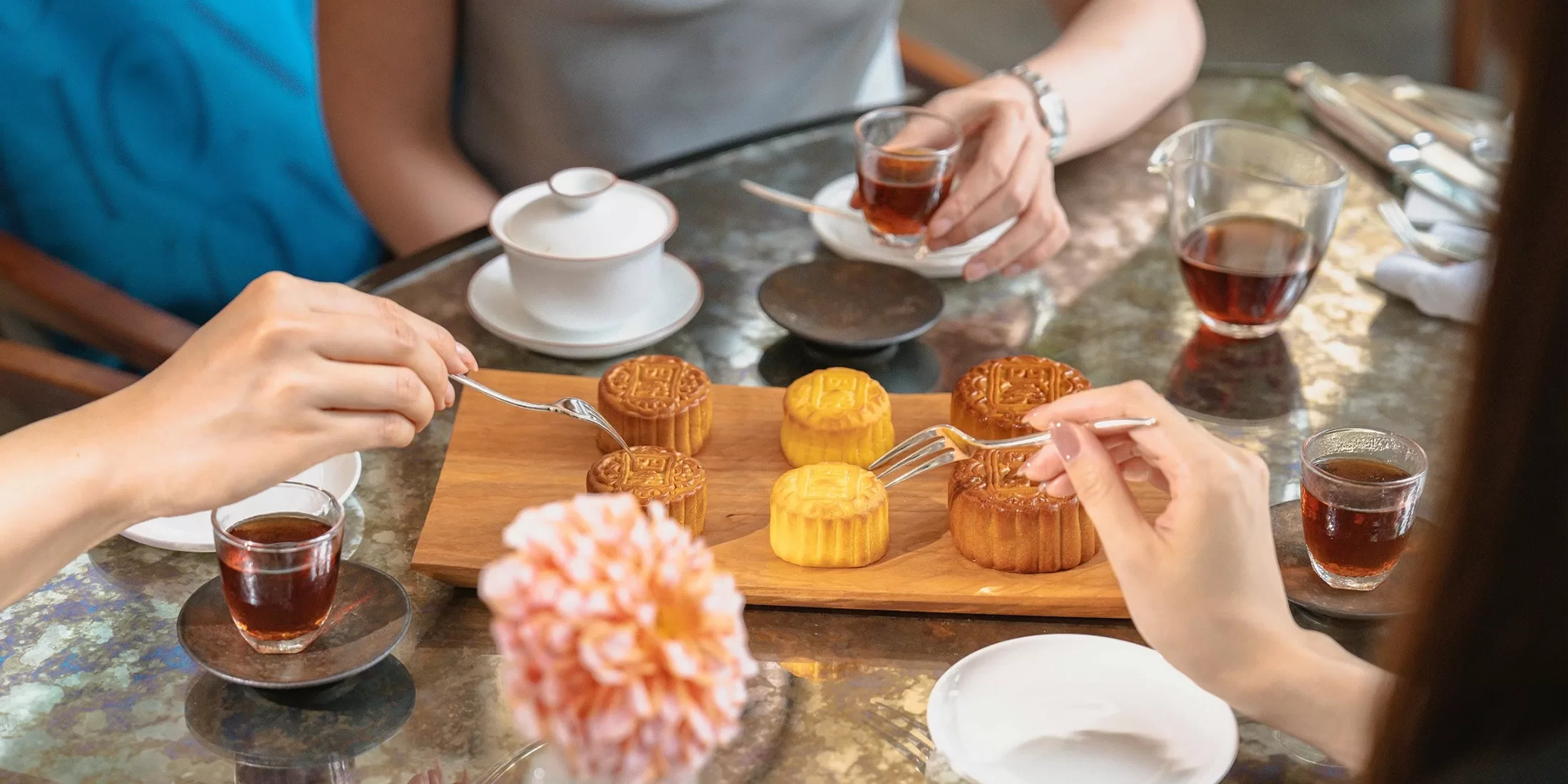 A group of people gathered around a table, enjoying mooncakes and cups of teas in Hong Kong.