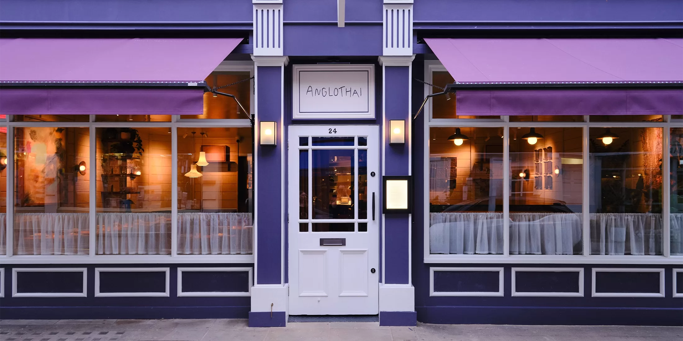 A purple storefront of new London restaurant, Anglothai with a white door centered between two large windows. The windows have lavender awnings above them and curtains inside. The building façade features decorative white trim.