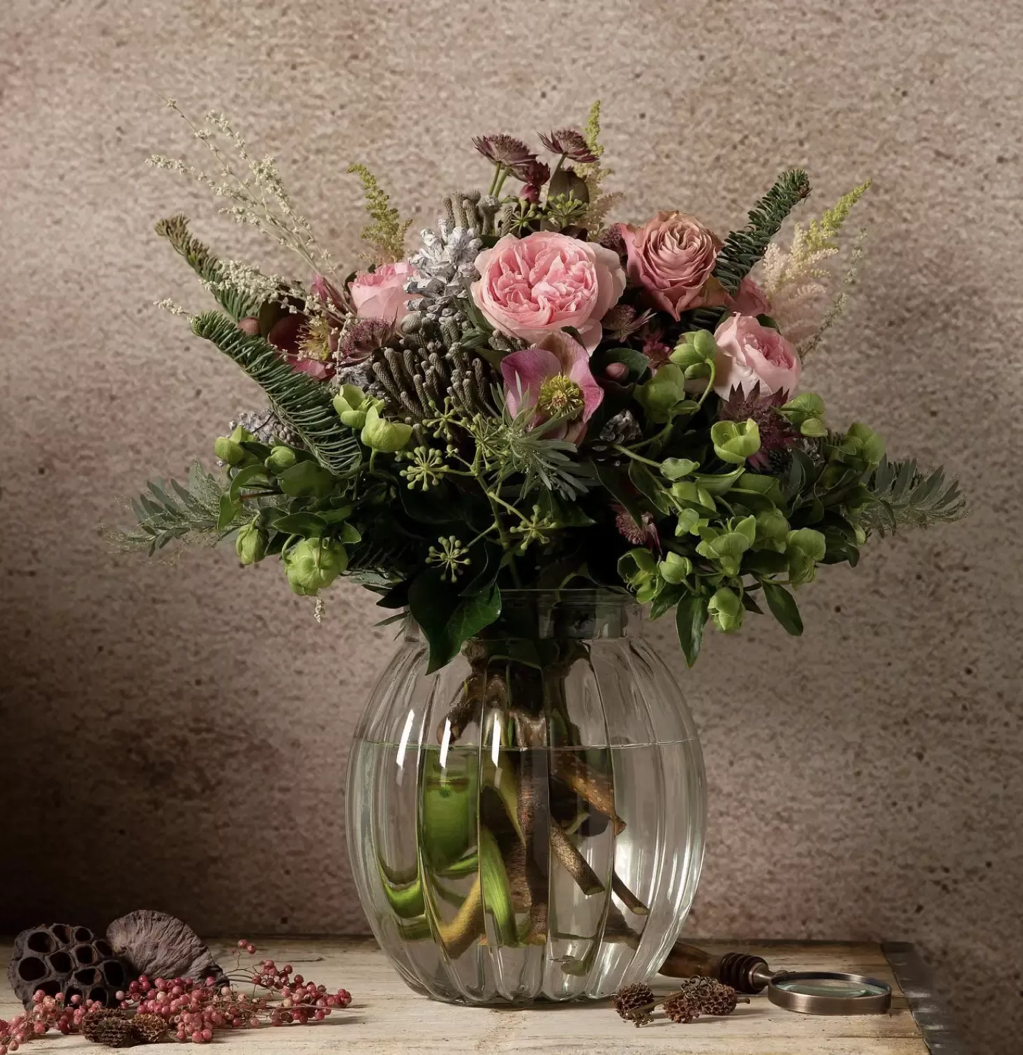 Photography of pink and green flowers in a glass vase in front of rustic wall at Ronnie Colby florist