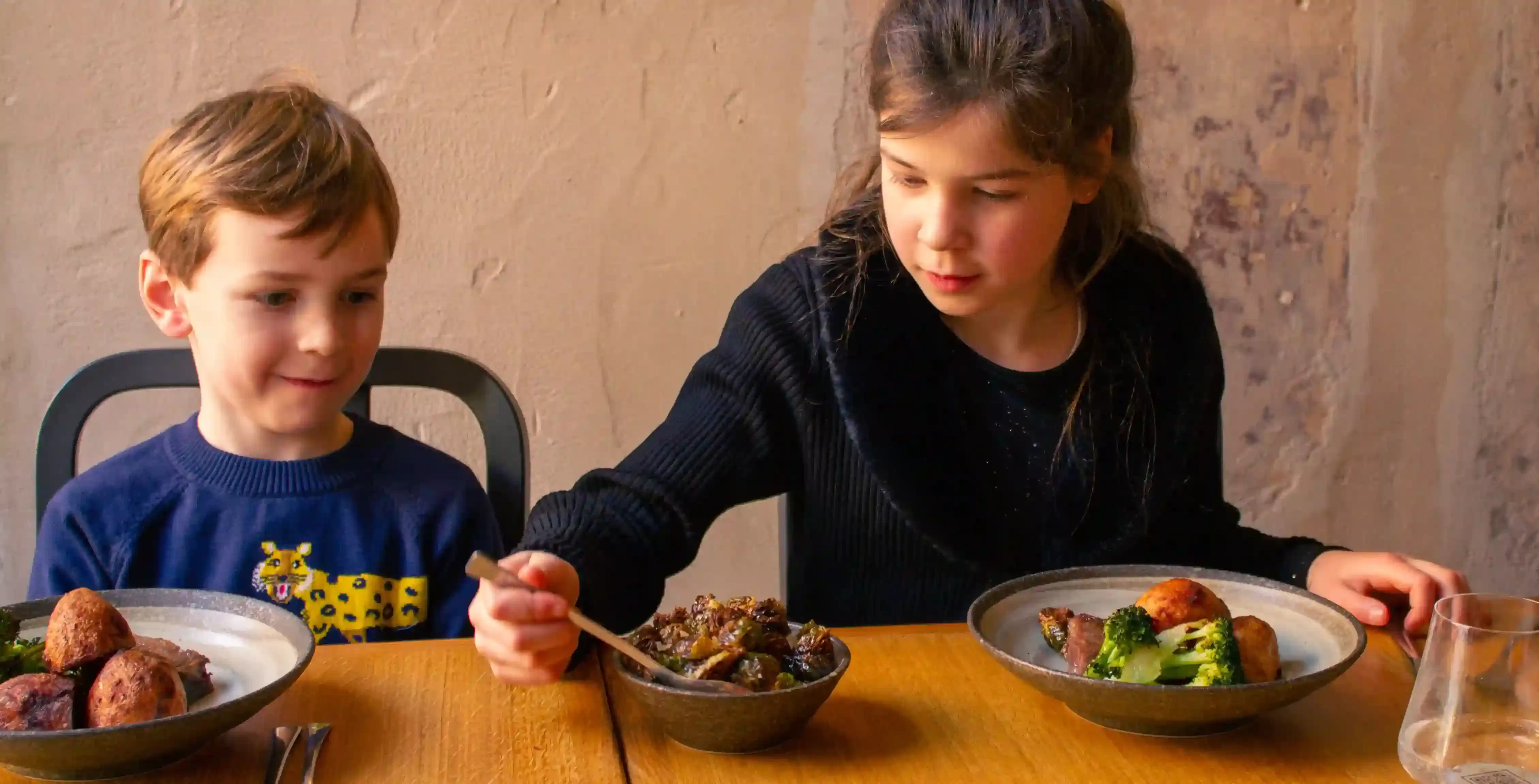 Two children sat at a table eating a selection of dishes
