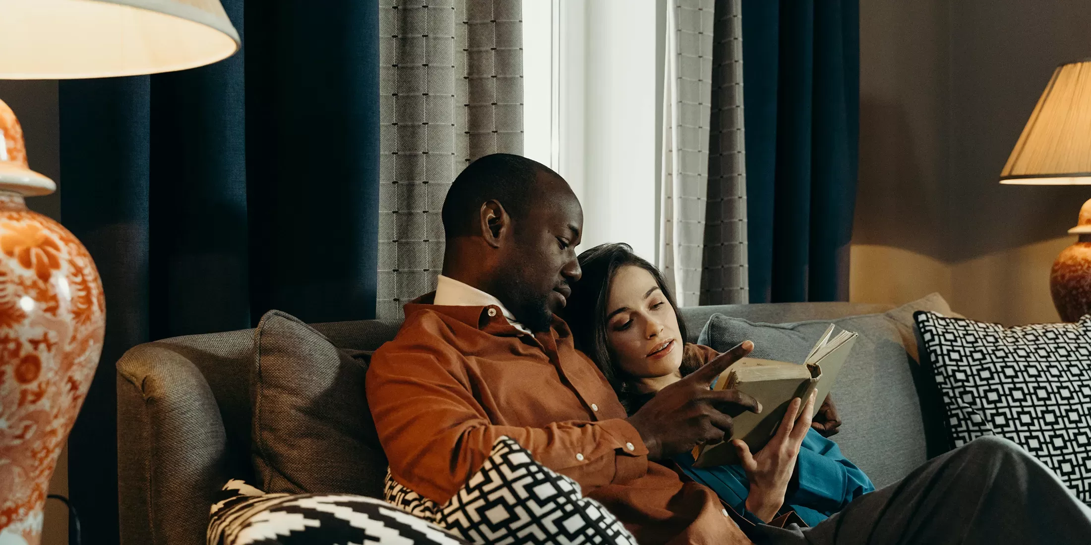 Man and women cuddling on a sofa in a living room reading a book