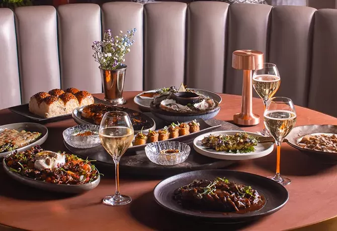 Display of Asian cuisine brunch served with champagne on a round table with pleated taupe sofa seating at CÉ LA VI, Dubai Downtown