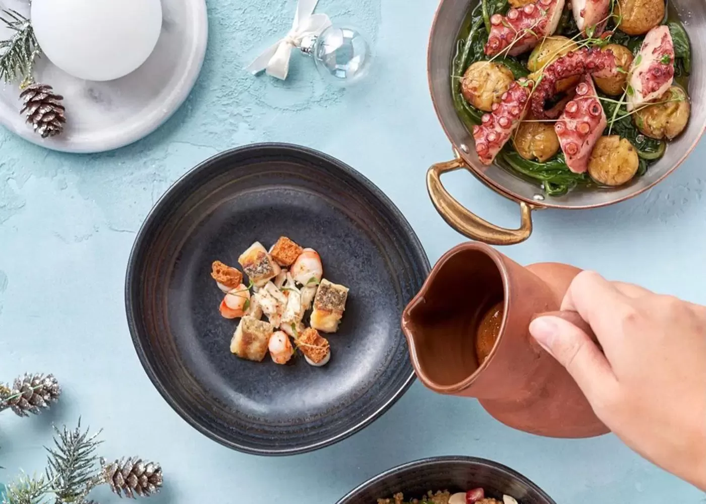 Person pouring sauce into dish in a round bowl with display of modern Portuguese cuisine at Tasca in the Mandarin Oriental Jumeirah, Dubai