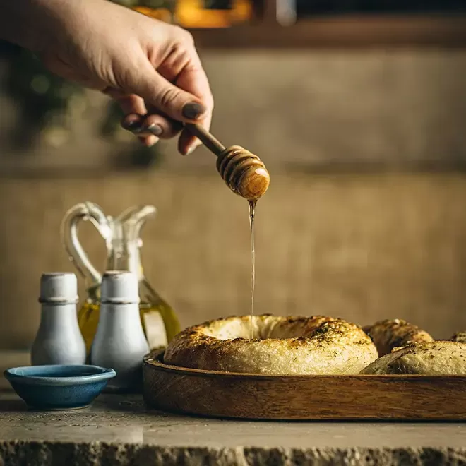 Person dripping honey on the famous wood-fried bread with truffle honey, chickpea miso butter at Jeru, Mayfair, London