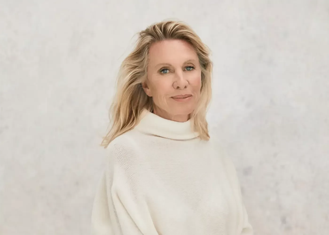 Photograph of Lady Banford sitting in front of a white background, with long blonde hair and wearing a cream turtle neck knitted jumper.