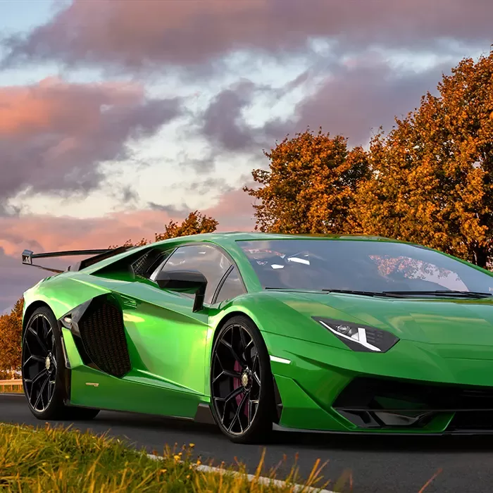 A shiny green sports car drives on a road bordered by grass and autumn trees under a partly cloudy sky at sunset.