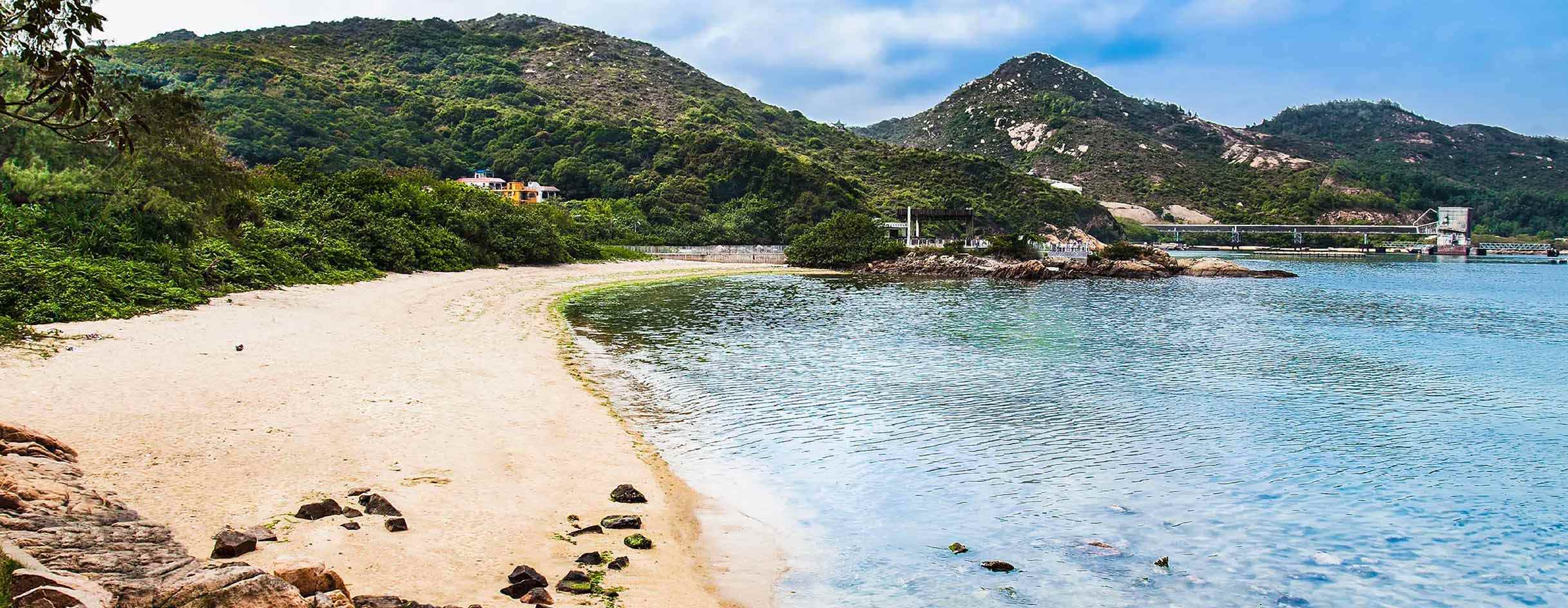 Golden beaches with blue sea surrounded by green hills.