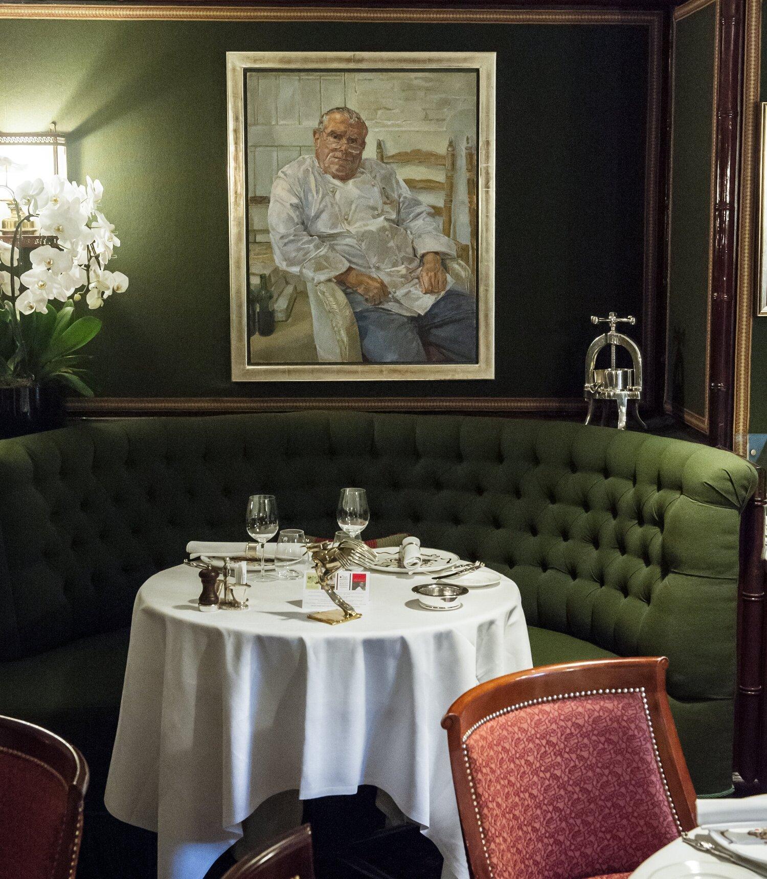 Restaurant dining booth with circular green sofa seating and rounded table in front of a portrait on a green wall