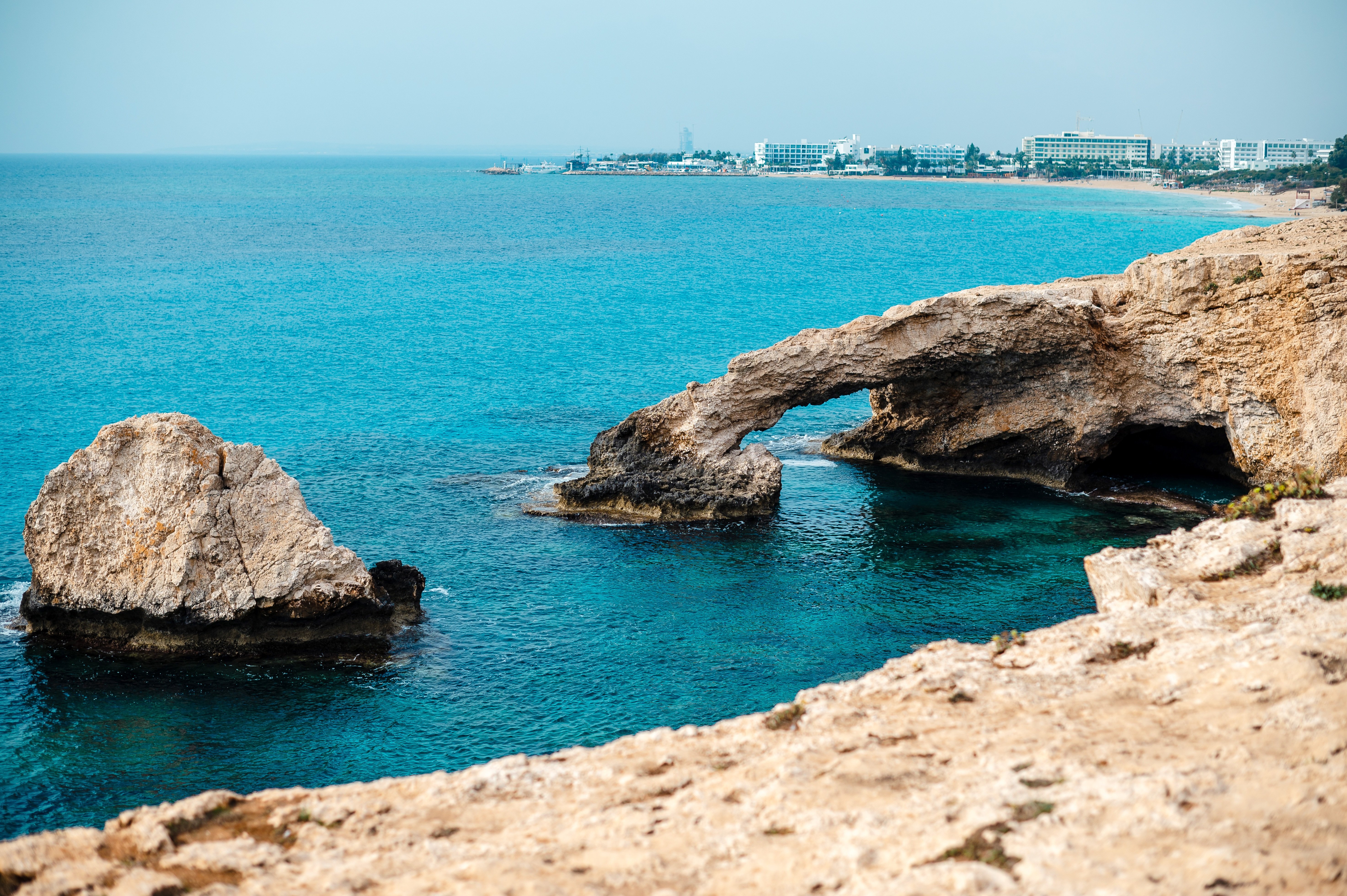 Lovers Bridge, a natural bridge shaped from the stone of the sea overlooking blue sea, beach and costal hotels in Ayia Napa