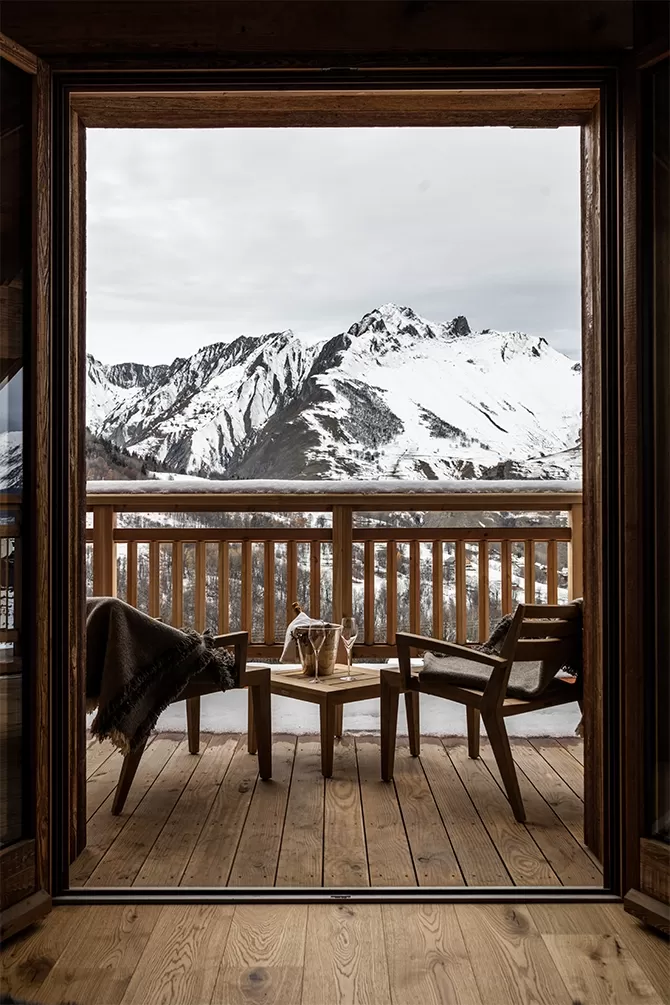 Wooden balcony with low lying chairs and coffee tables with a view on the snowy mountains at M Lodge & Spa, Saint Martin de Belleville