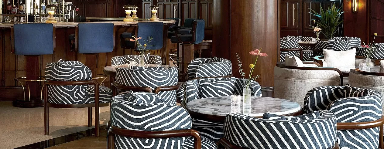 Grand bar lounge with blue stools and black and white printed chairs in seating area