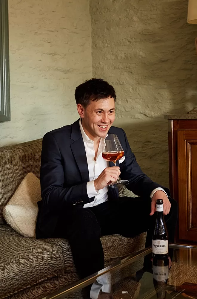 Nick Showering sat in a suit on a sofa drinking Showering cider