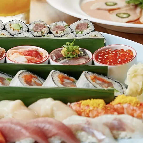 Assorted sushi platter featuring rolls with tuna, salmon, and avocado, alongside various nigiri and sashimi pieces. Small bowls of roe and pickled ginger accompany the sushi, with a focus on the colorful and fresh presentation at Nobu, London.
