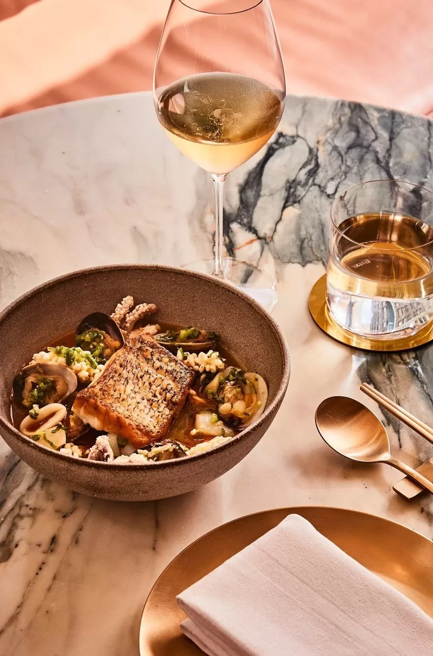 Seafood ramen served in bowl with wine and gold plates on marbled table at Oiji Mi, Flatiron, New York