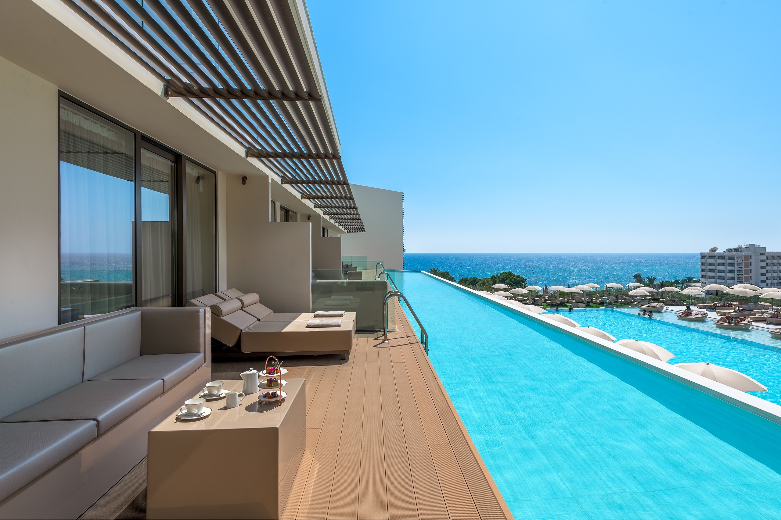 Luxurious hotel suite balcony with cream sofa and sunbeds with long private pool overlooking the hotel pool, costal hotels and sea view.