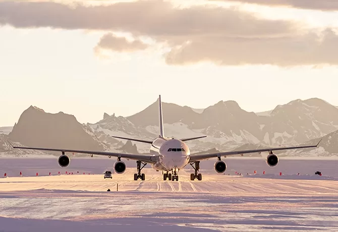 Private plane taking off on runway with pink skies and mountains behind