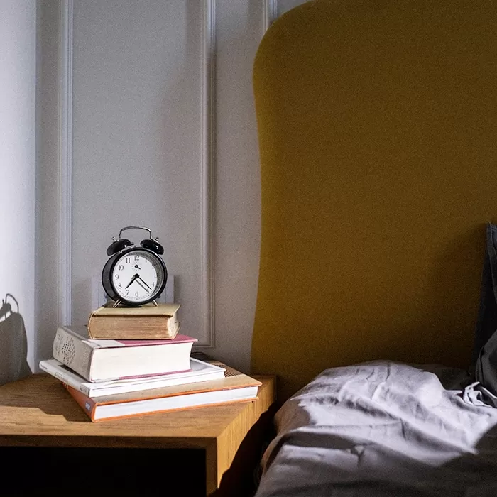 Stack of books and a clock on a bedside table next to a bed